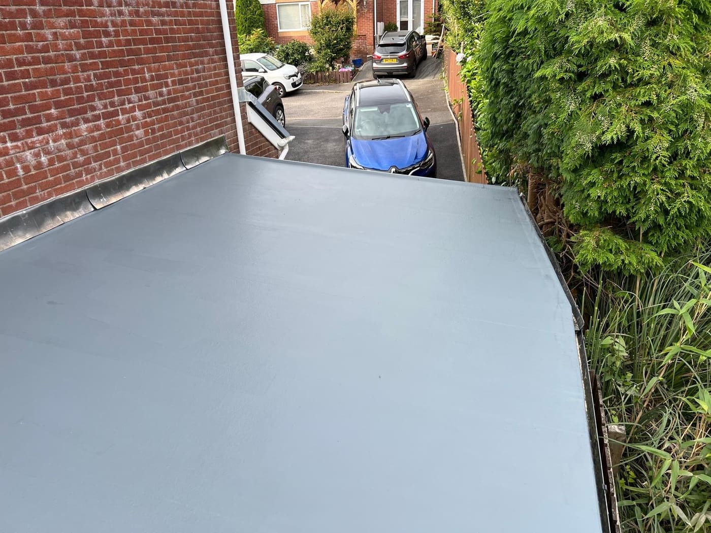 New light-grey flat roof on a side extension beside a driveway